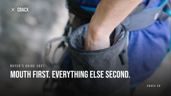 A climber reaching into a worn grey chalk bag clipped to a harness, hand buried past the knuckles in a narrow opening