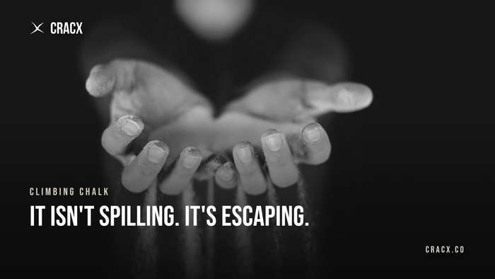 Climbing chalk streaming out between a climber's fingers against a dark background