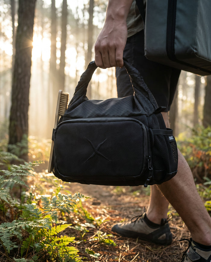 A climber carrying the CRACX Ascend by its handle on a forest trail at dawn, crash pad on the back