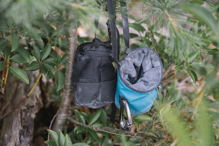 Two chalk bags hanging from a branch at the base of a boulder