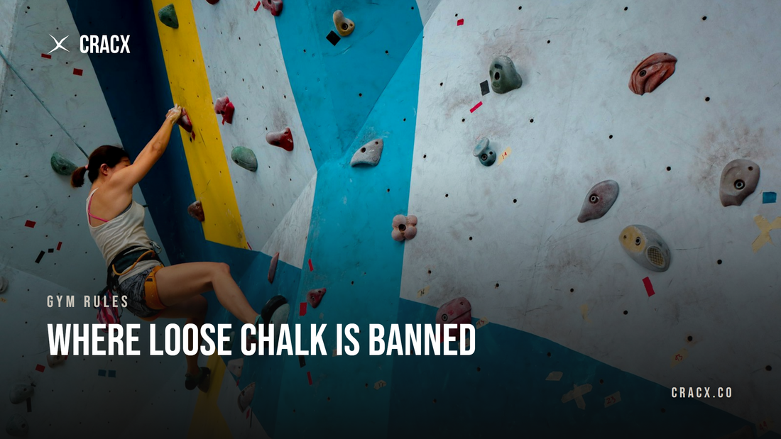 A boulderer with chalked hands mid-move on an indoor gym wall, chalk bag on her waist