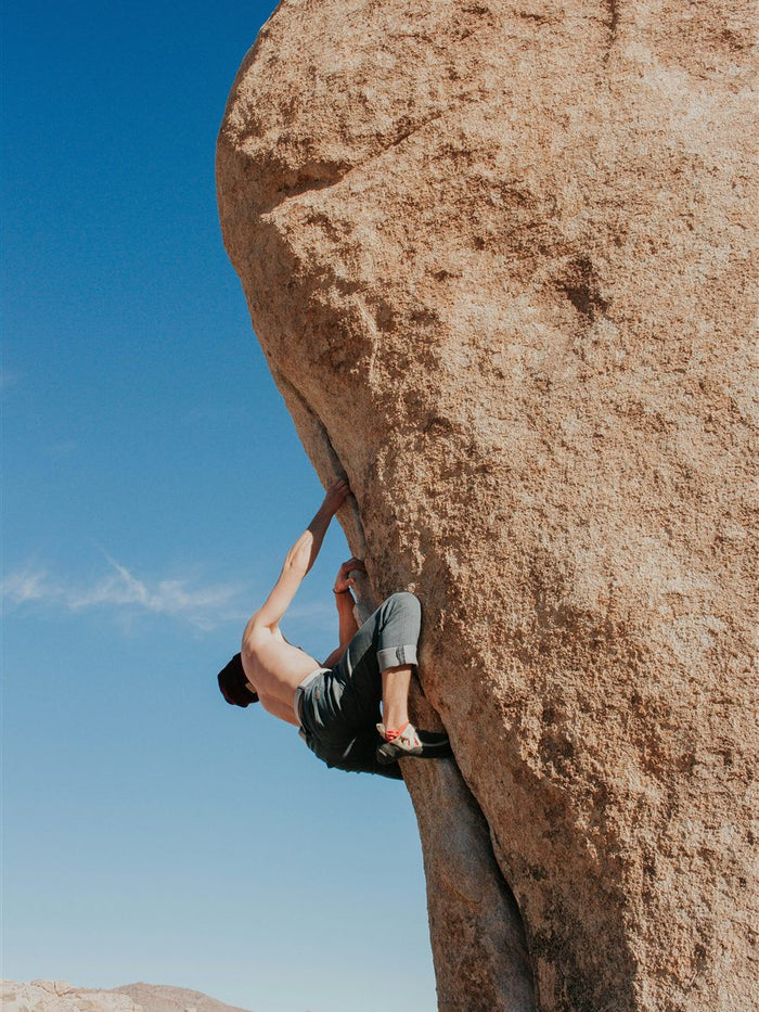 Boulderer pulling over the lip of a desert highball, the kind of outdoor session you carry a bouldering chalk bucket into