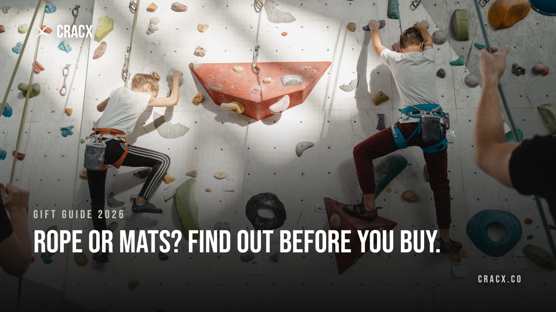 Two young climbers on a top-rope wall at an indoor climbing gym, each wearing a harness with a chalk bag clipped on, while belayers hold the ropes