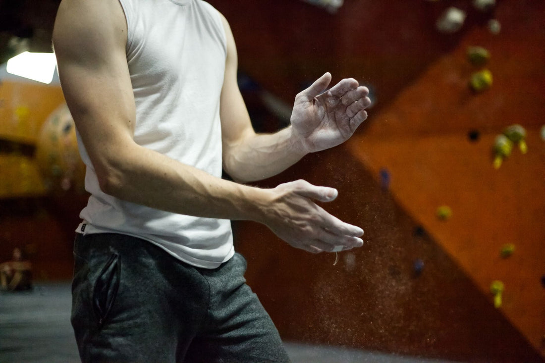 A boulderer clapping chalk off his hands in front of a bouldering wall