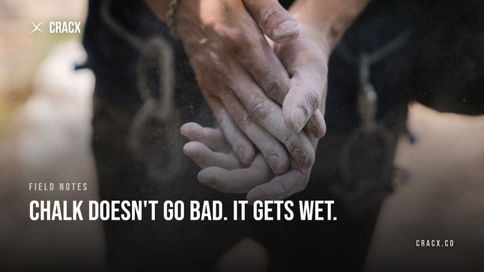 Close-up of a climber rubbing chalked hands together outdoors, a cloud of fine dry chalk dust drifting in the air