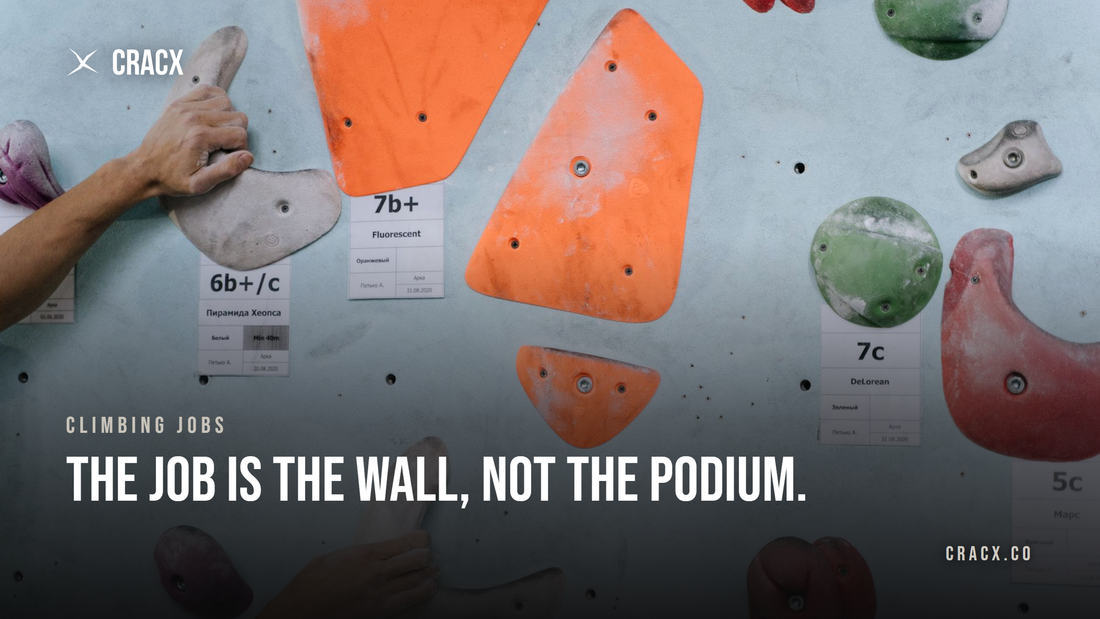 Two hands gripping holds on a bouldering wall covered in labeled problem tags with grades