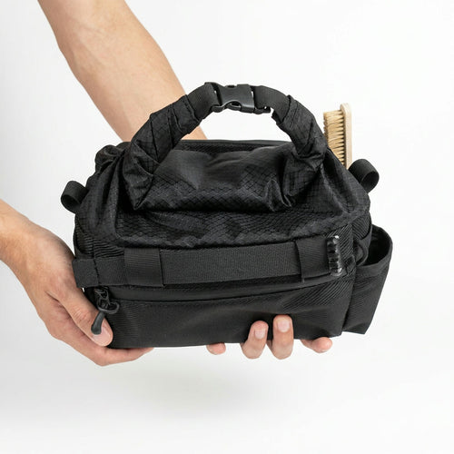 Hands holding the rolled top of the CRACX Ascend, the trident buckle clipped at the centre of the handle