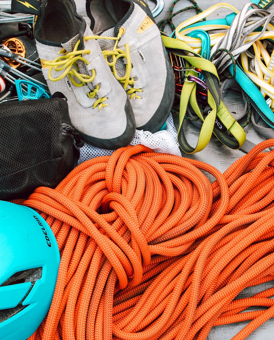 A pile of climbing gear spread out: ropes, quickdraws, climbing shoes and a helmet, everything loose