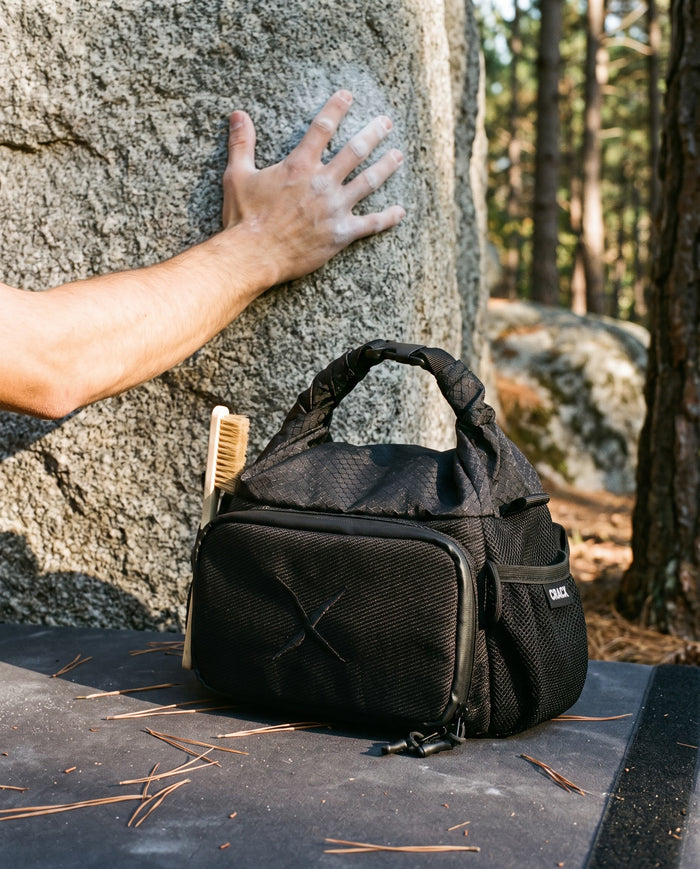 The CRACX Ascend on a crash pad at the base of a granite boulder, a chalked hand on the rock
