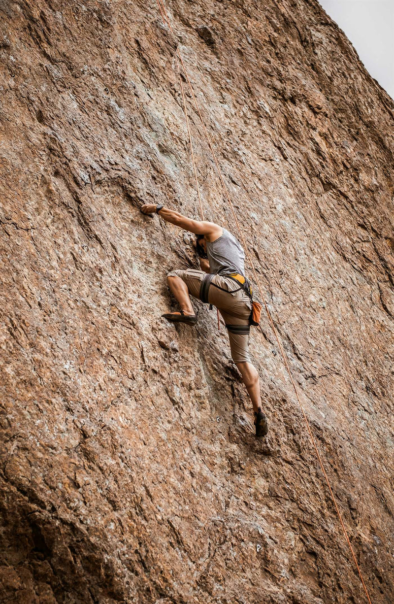 A climber high on a steep sunlit granite wall, chalk marks on the holds